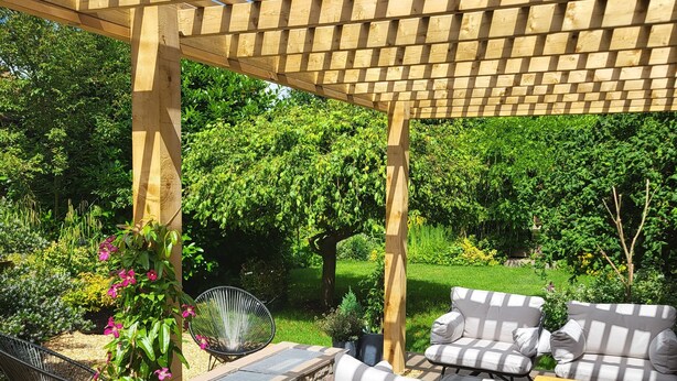 A wooden pergola structure with outdoor seating, including a table and chairs, surrounded by a garden with various plants and a lawn. - Field View B&B (Goole)