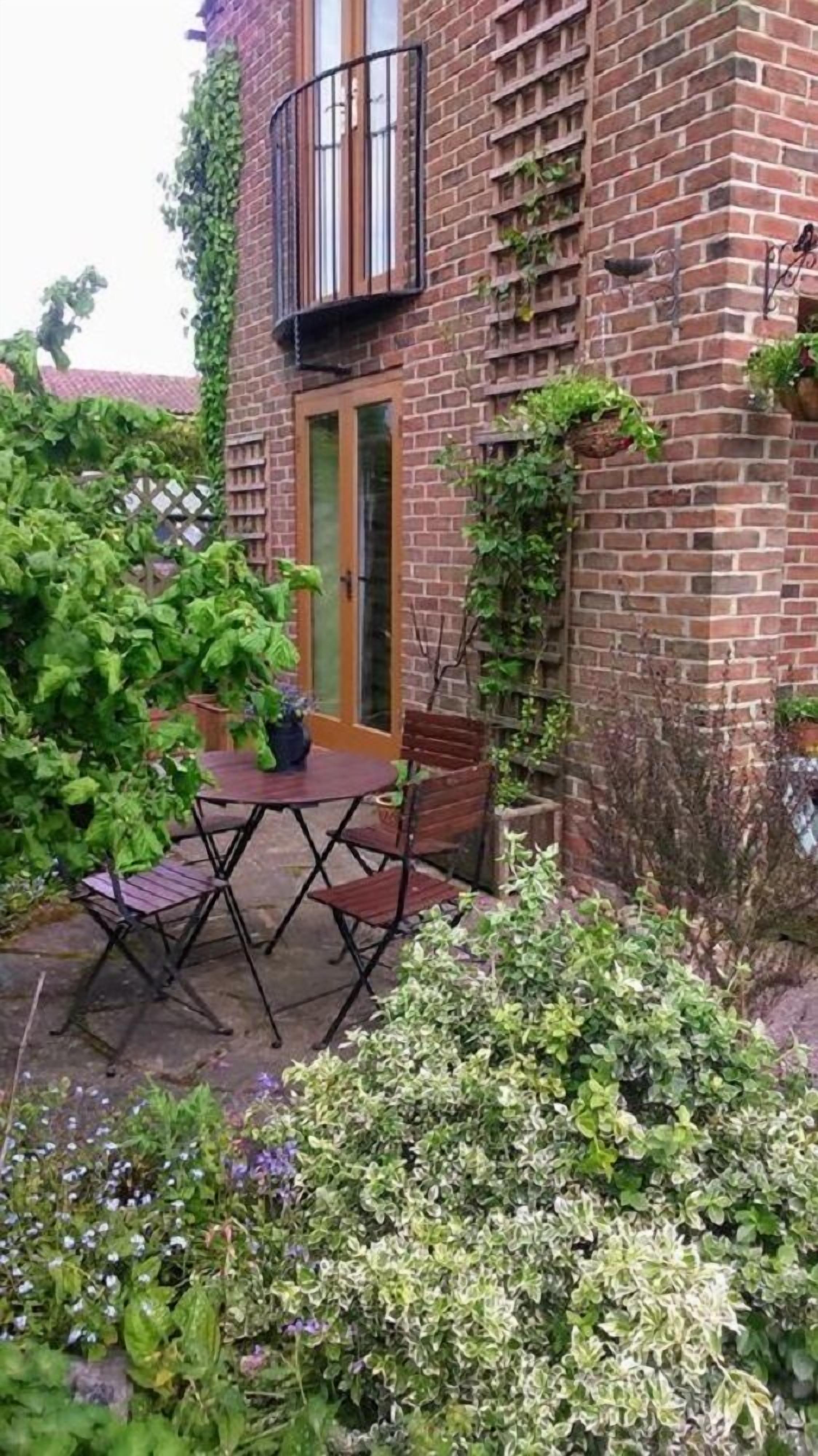 A brick building with a door, a small balcony, and a patio area with a table and chairs.