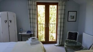A room with two beds, a table with a chair, a radiator, and a window with curtains. - Field View B&B (Goole)