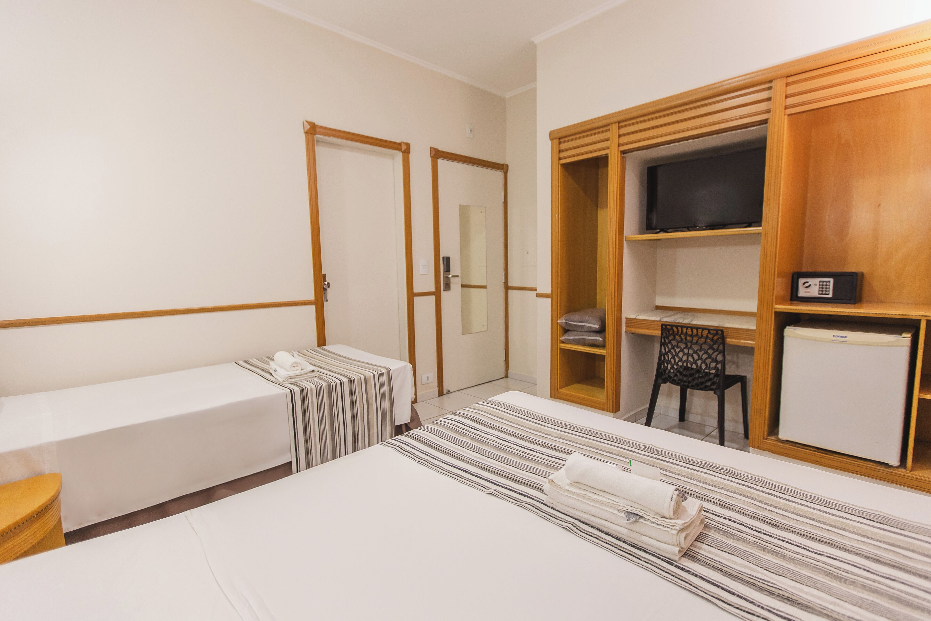 Habitació d'hotel amb un llit, una taula petita, una cadira, un armari i una televisió.