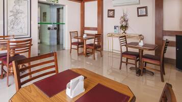 Un comedor de hotel con mesas y sillas de madera, una obra de arte enmarcada en la pared y un letrero de salida verde.
