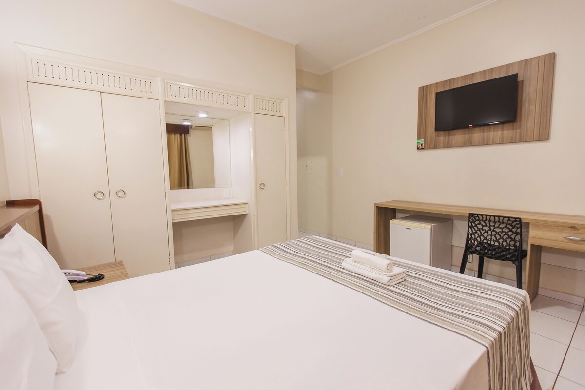 Una habitación de hotel con cama, escritorio, silla, televisor y armario.