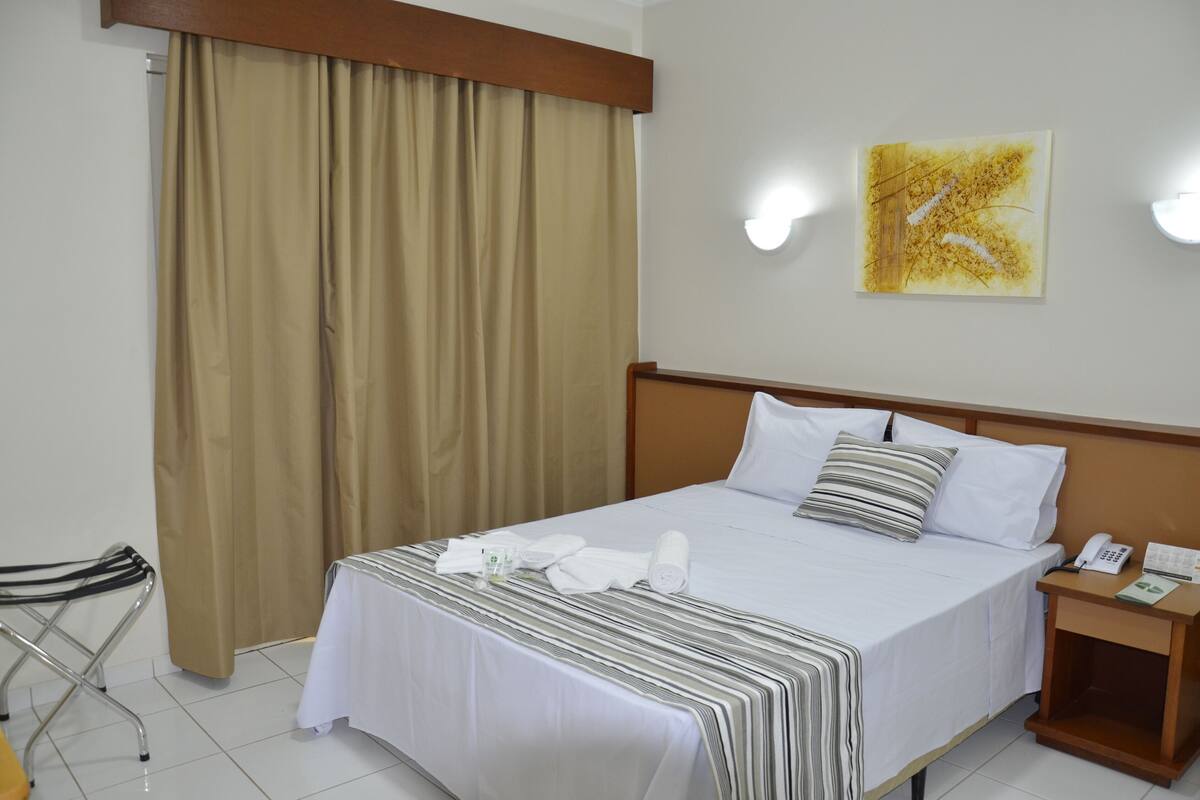 Ein Hotelzimmer mit einem Bett, einem Nachttisch mit Telefon, einem Vorhang und einem Wandbild.