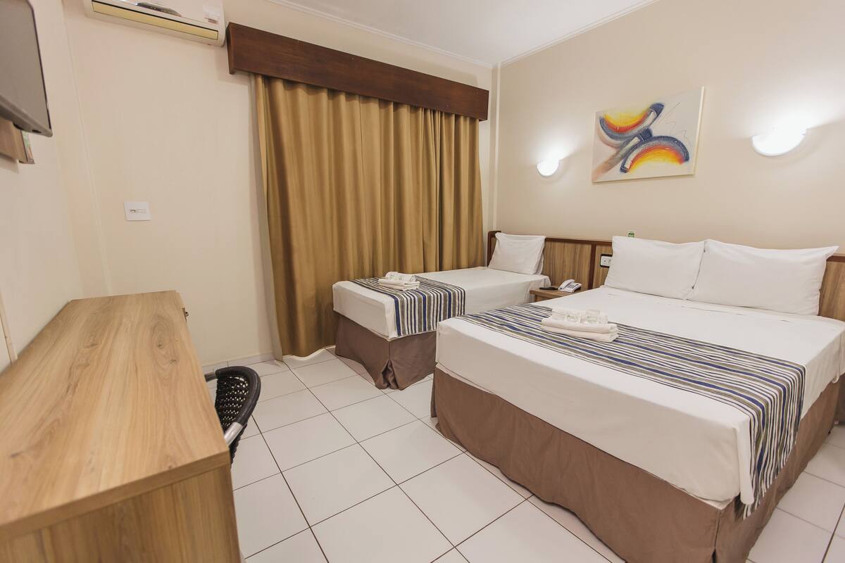 Ein Hotelzimmer mit zwei Betten, einem Schreibtisch und einem großen Fenster mit Vorhängen.