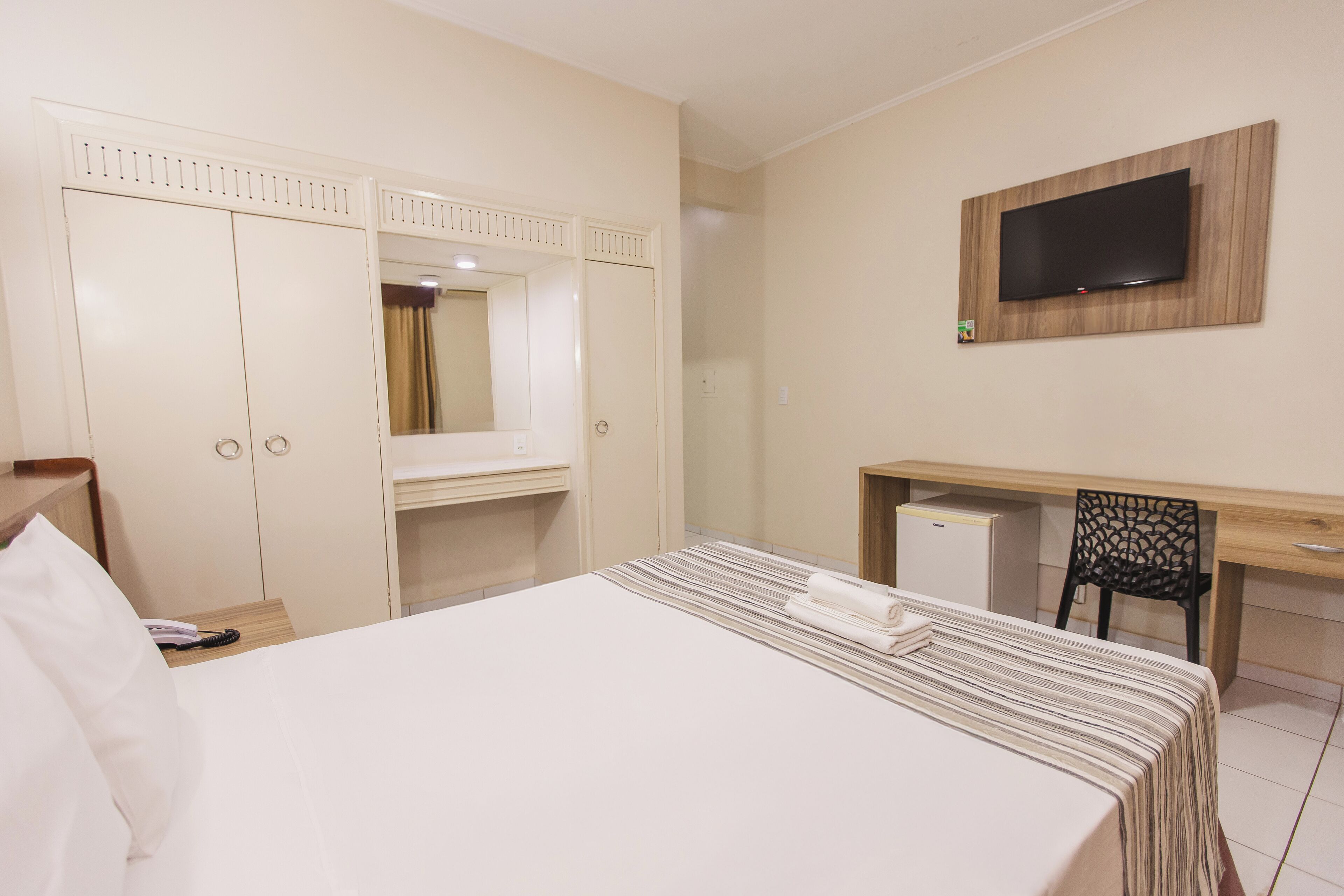 A hotel room with a bed, a desk, a chair, a TV, and a wardrobe.