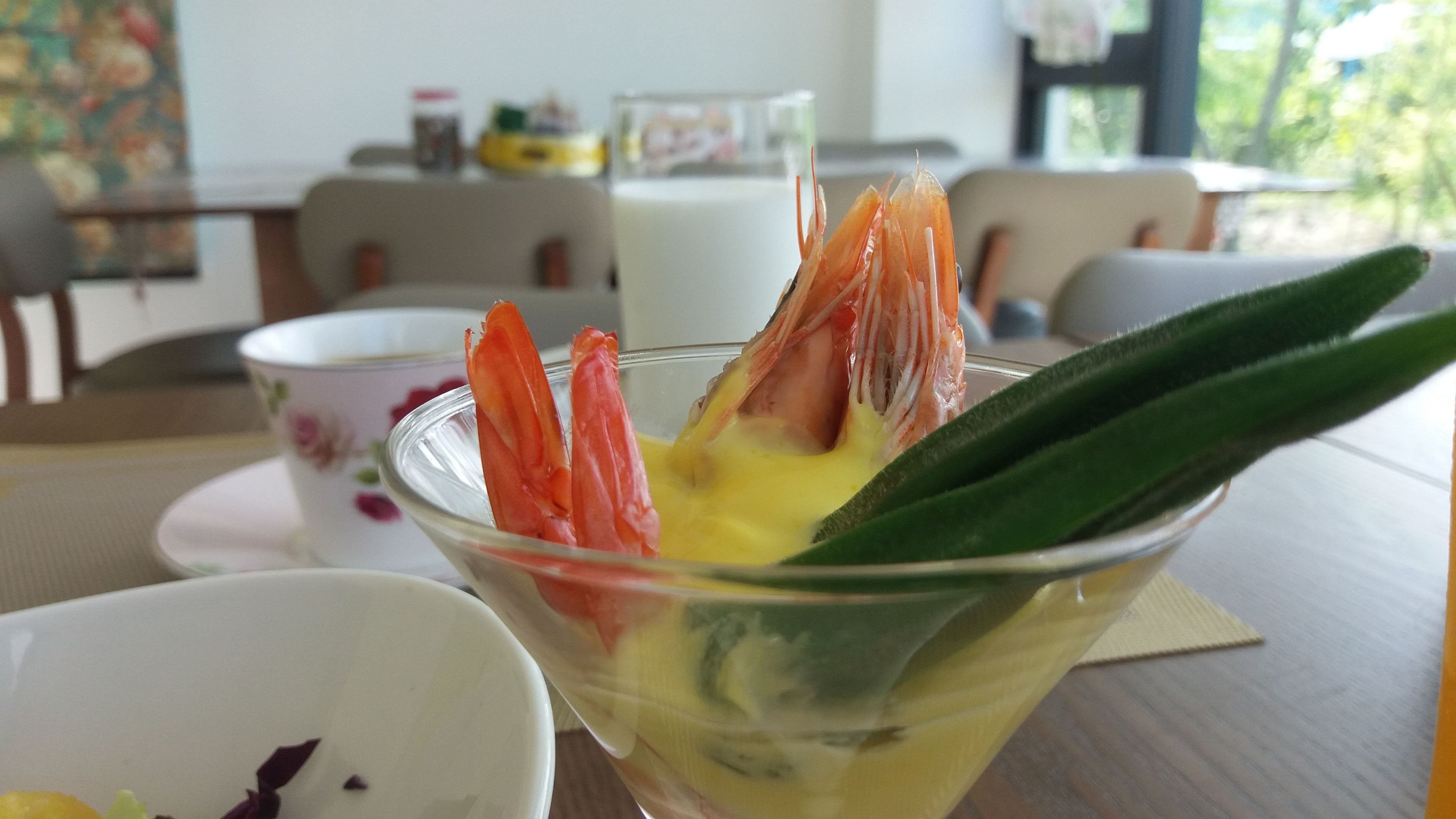 A glass bowl with a shrimp cocktail and a green vegetable on a table.