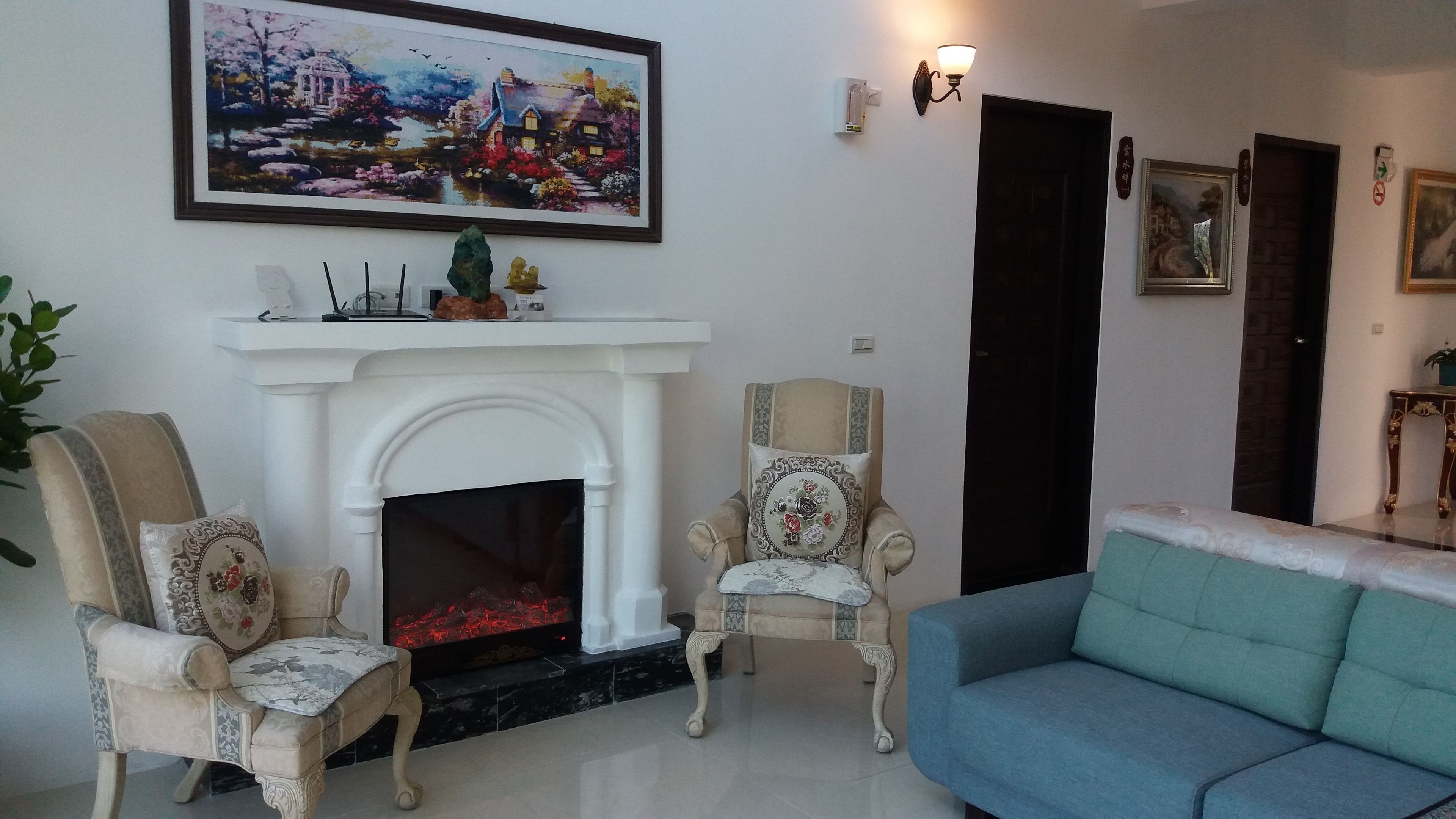 A living room with a fireplace, two armchairs, a sofa, and a painting above the fireplace.
