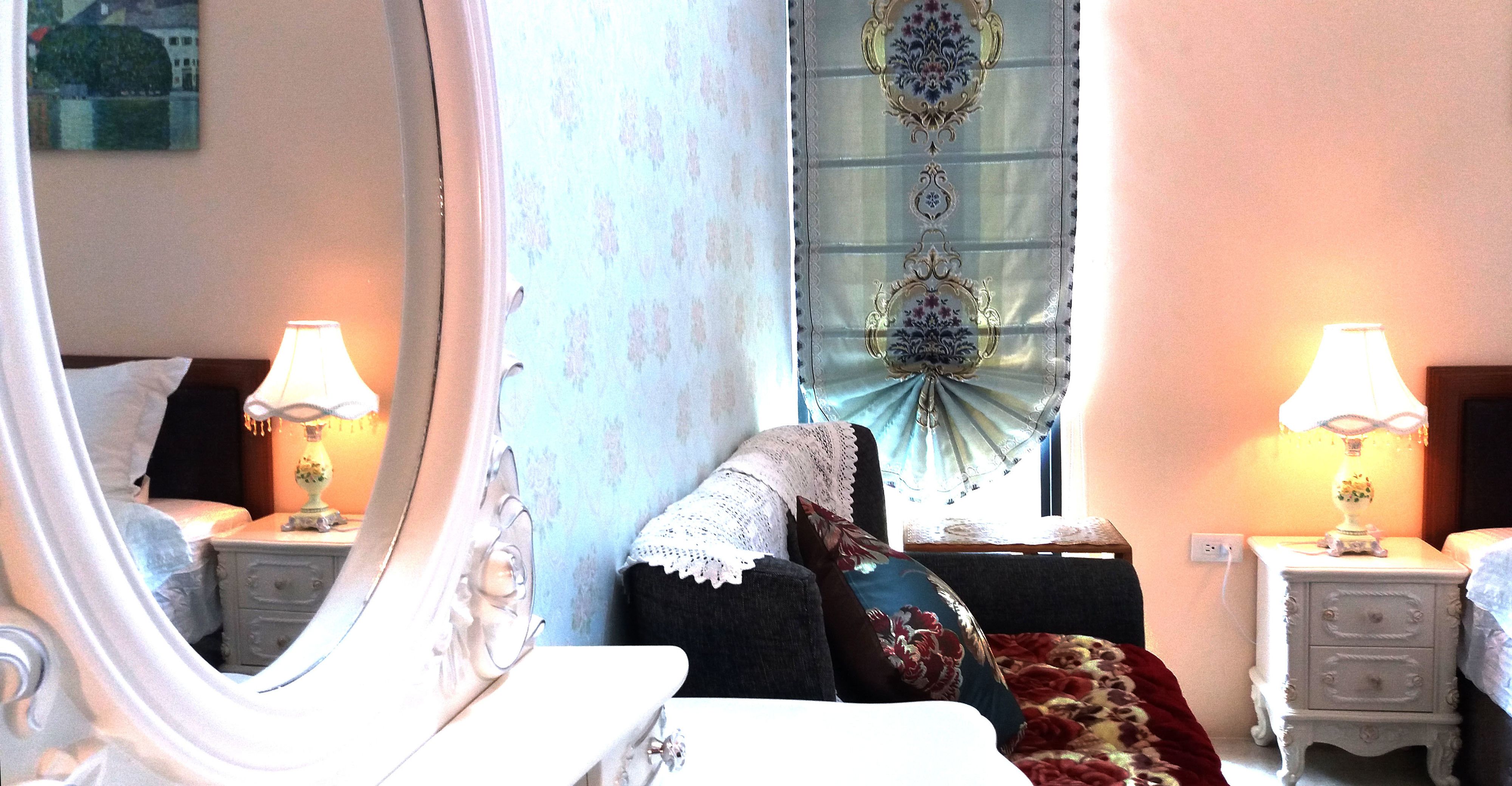 A bedroom with a bed, two bedside tables with lamps, a window with curtains, and a mirror.