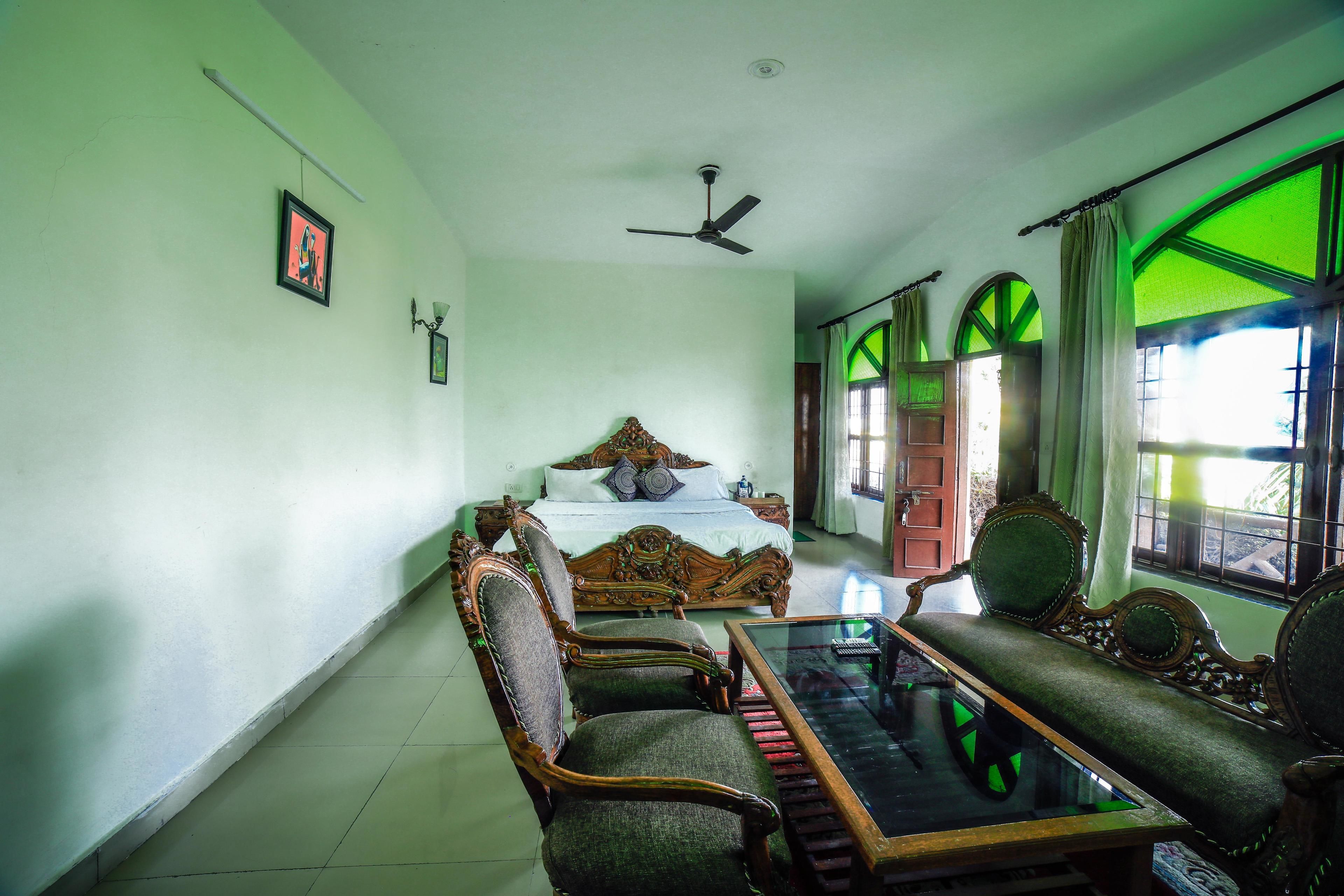 A bedroom with a bed, two chairs, a table, and a ceiling fan.