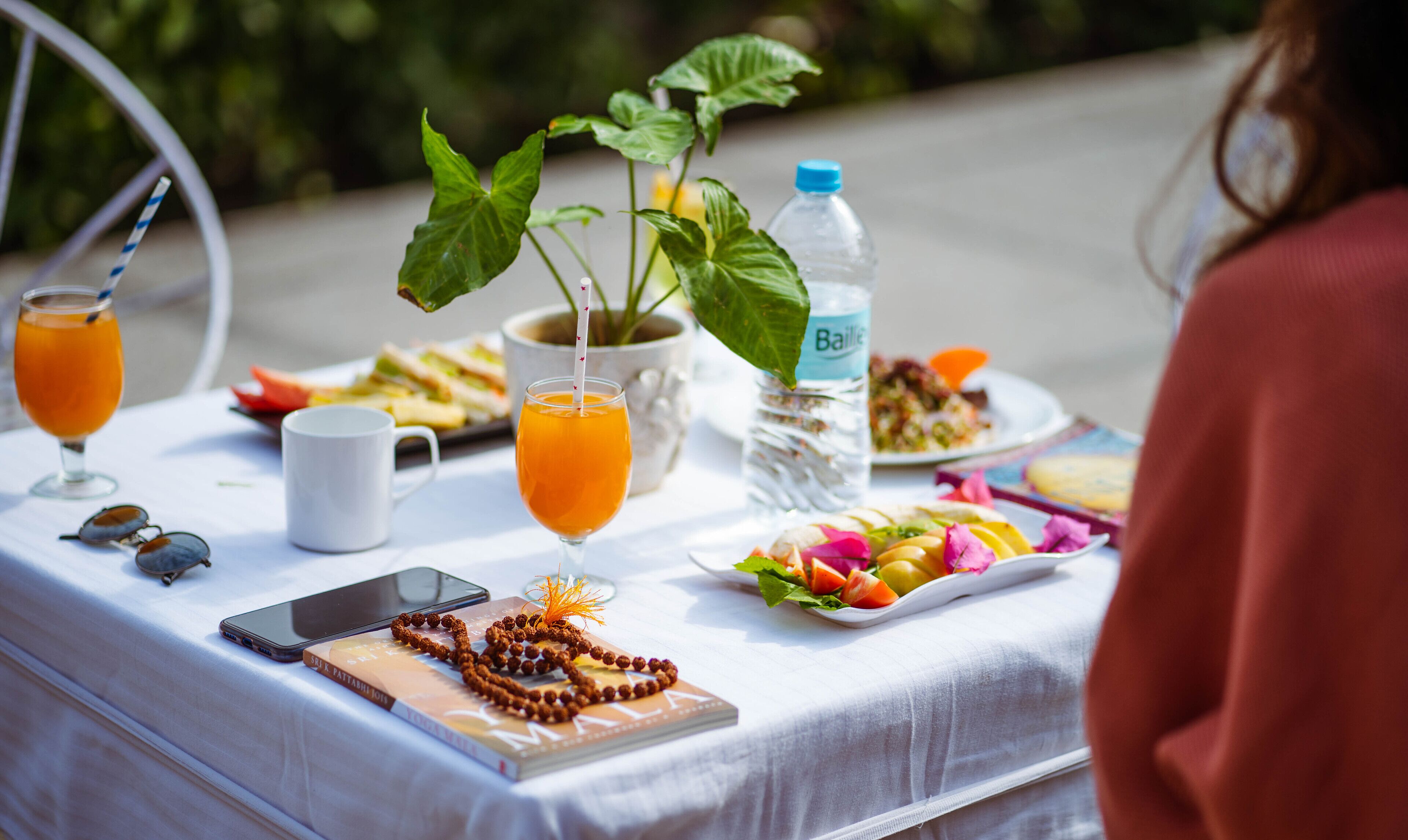 A table set with a drink, a smartphone, a book, a rosary, and a plate of fruit.
