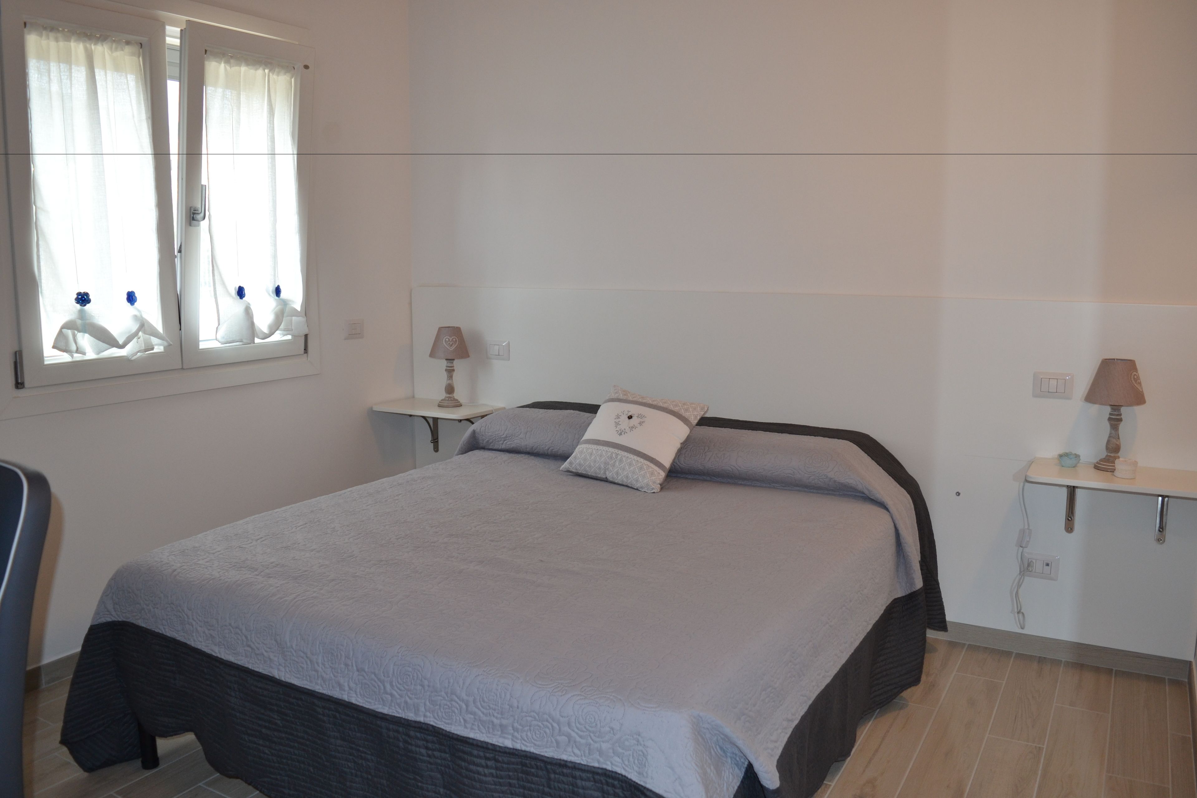 Una camera da letto con un letto, due comodini, uno specchio e una finestra con tende.