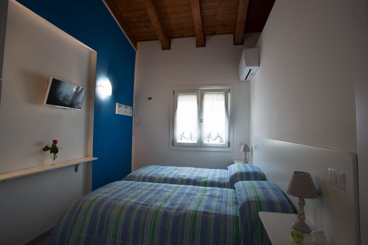 Un dormitorio con dos camas, televisión en la pared, una ventana y una lámpara en la mesita de noche.