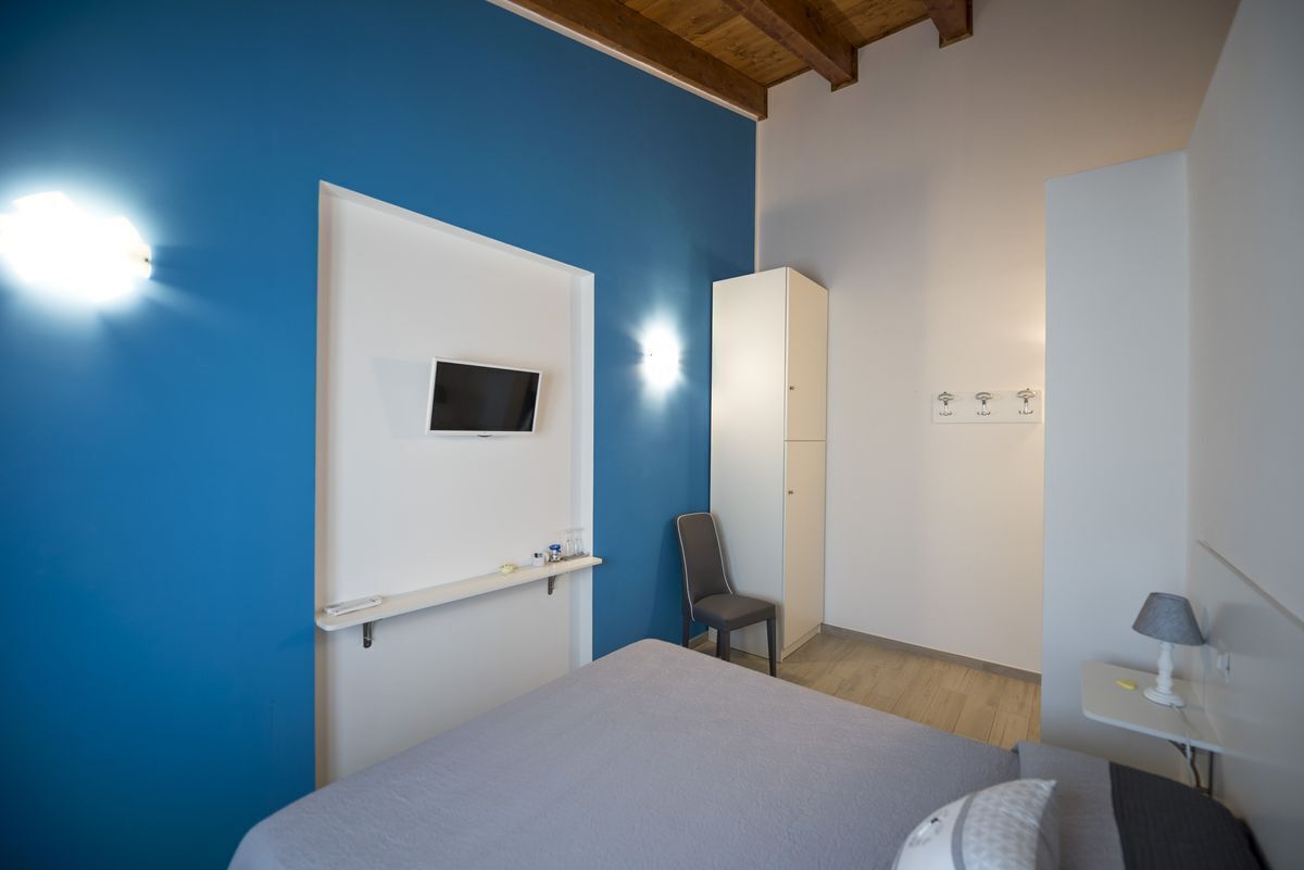 A bedroom with a bed, a chair, a TV mounted on the wall, a wardrobe, and a bedside table with a lamp.