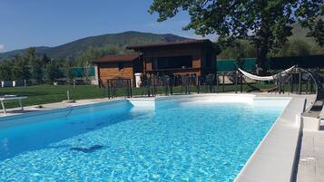 Ein klares Schwimmbecken mit einer Holzterrasse, einer Hängematte und einem Gebäude im Hintergrund.