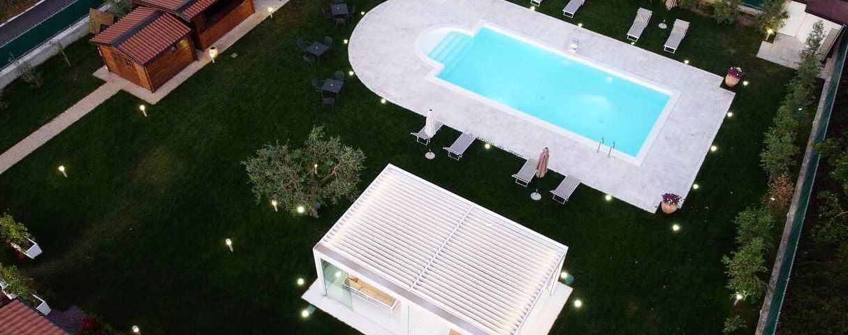 Vista aérea de una propiedad con piscina, sillas de descanso y un pequeño edificio.
