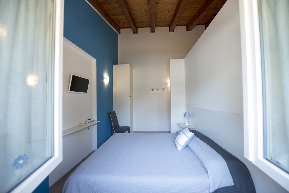 A bedroom with a bed, a TV mounted on the wall, a chair, and a bedside table with a lamp.