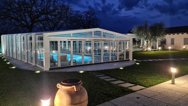 A glass-enclosed pool area with a clear view of the pool, surrounded by a well-lit patio and a large urn in the foreground. - Il Rifugio Del Tempo (Roccasecca)