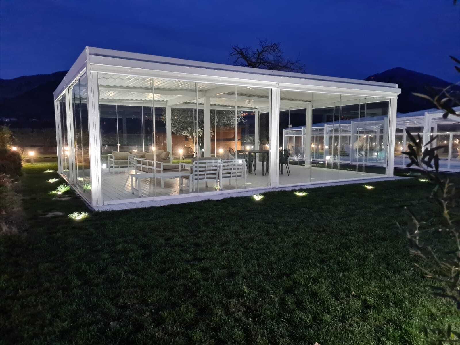 Una estructura moderna de vidrio con asientos y mesas, rodeada de caminos bien iluminados.
