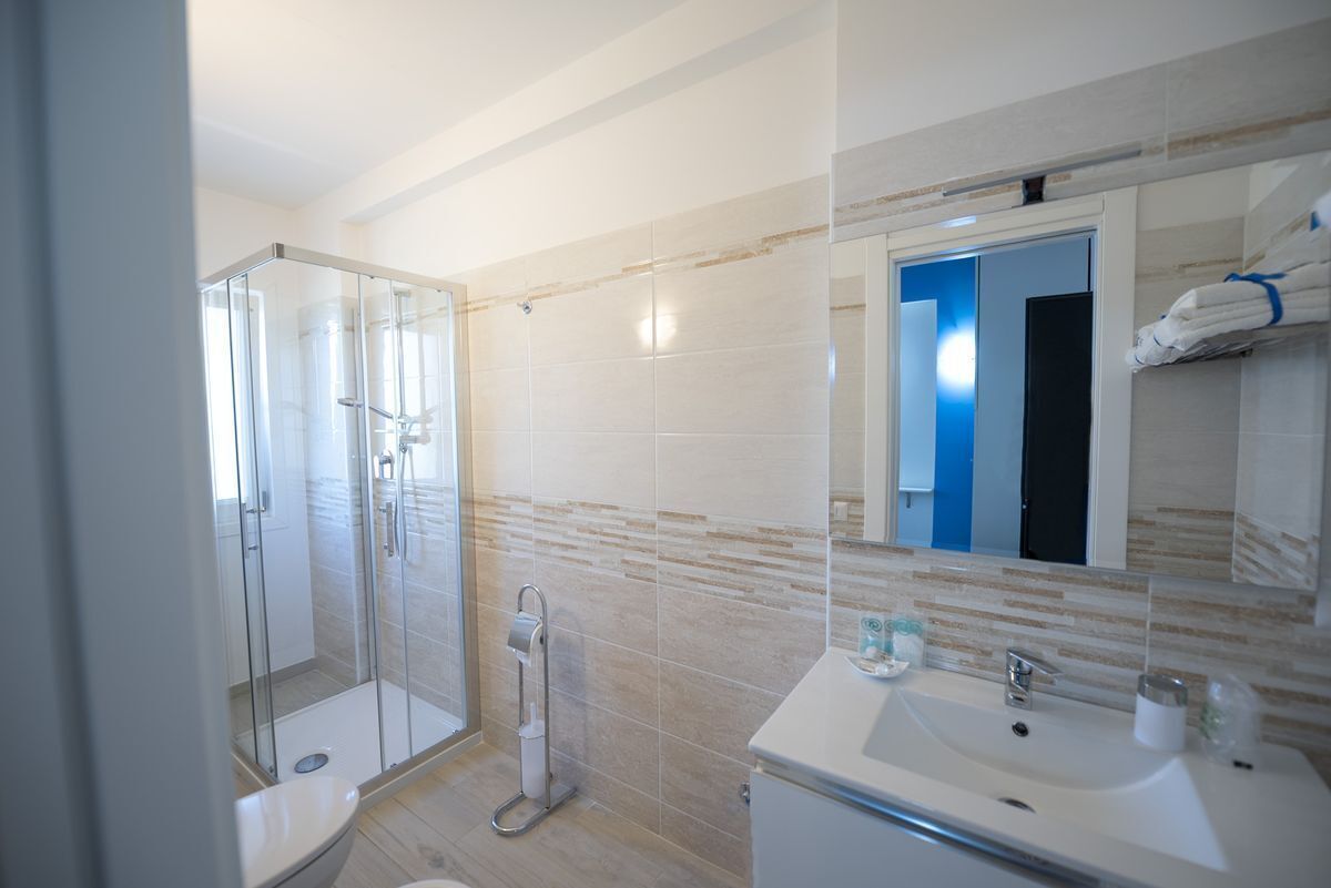 Un baño moderno con cabina de ducha de vidrio, lavabo blanco y espejo, con una puerta azul al fondo.