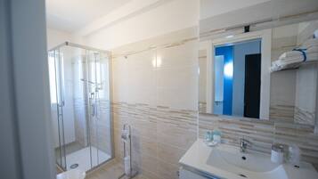 Une salle de bain moderne avec une douche à parois de verre, un lavabo blanc et un miroir dont la porte est bleue, visible à l’arrière-plan.