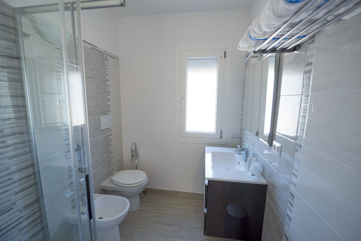 Ein modernes Badezimmer mit Duschkabine aus Glas, Toilette und Waschbecken mit Spiegel darüber.