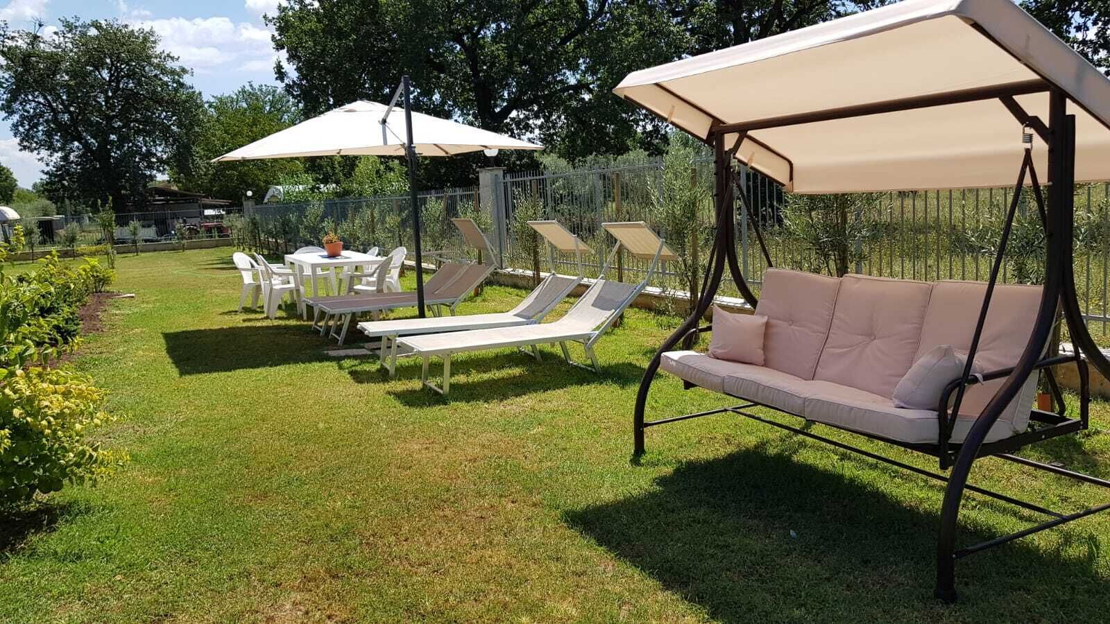 Un jardín con una silla columpio, tumbonas y una mesa con sillas.
