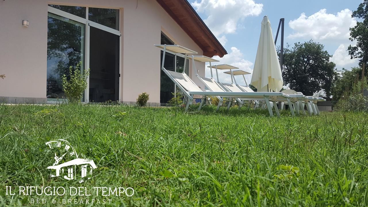 Un edificio moderno con ingresso in vetro, posti a sedere all'aperto con ombrelloni e il logo del bed and breakfast 'Il Rifugio Del Tempo'.