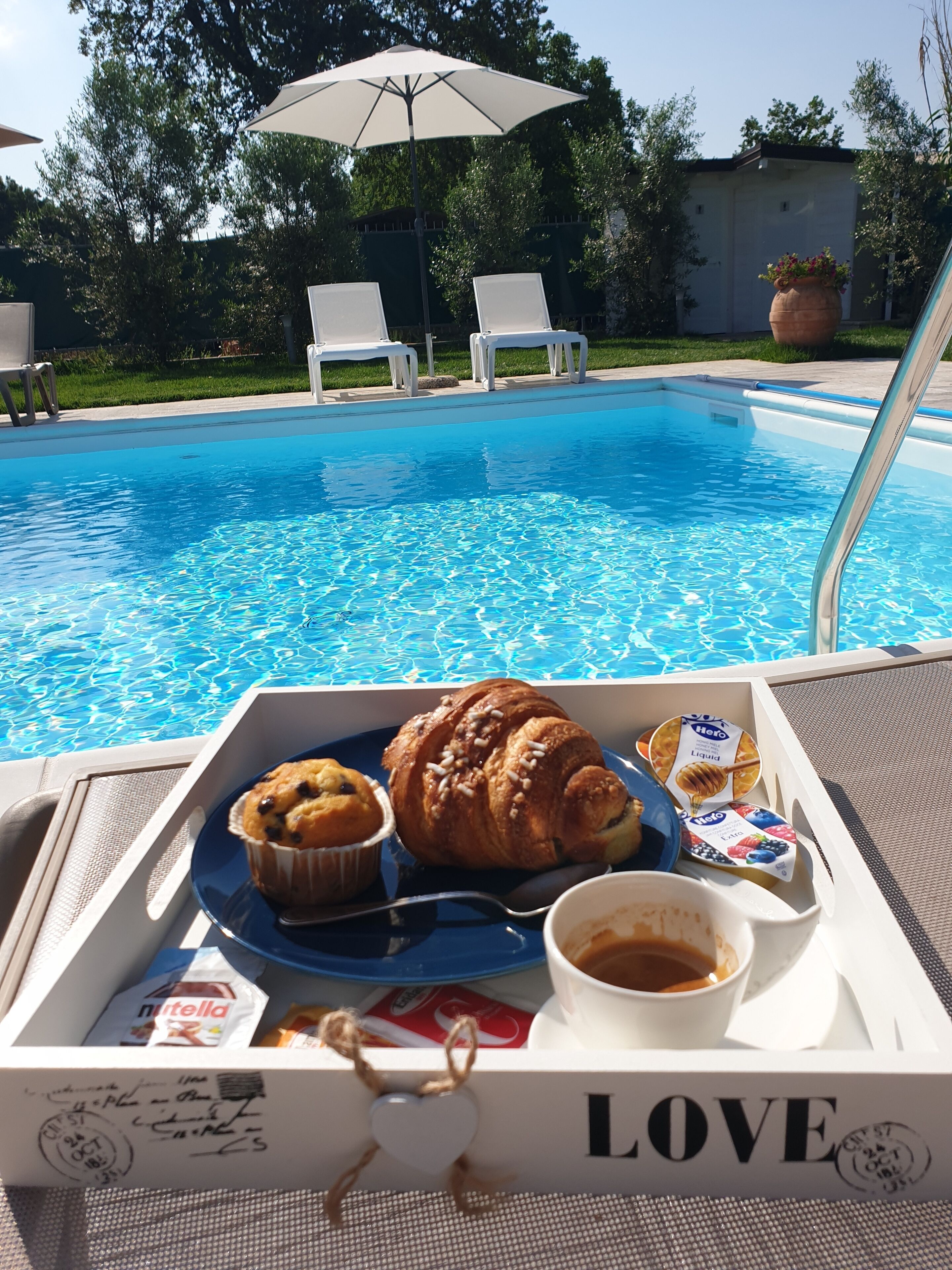 A tray with food items near a poolside, including a muffin, croissant, and yogurt, with a 'LOVE' sign on the tray.