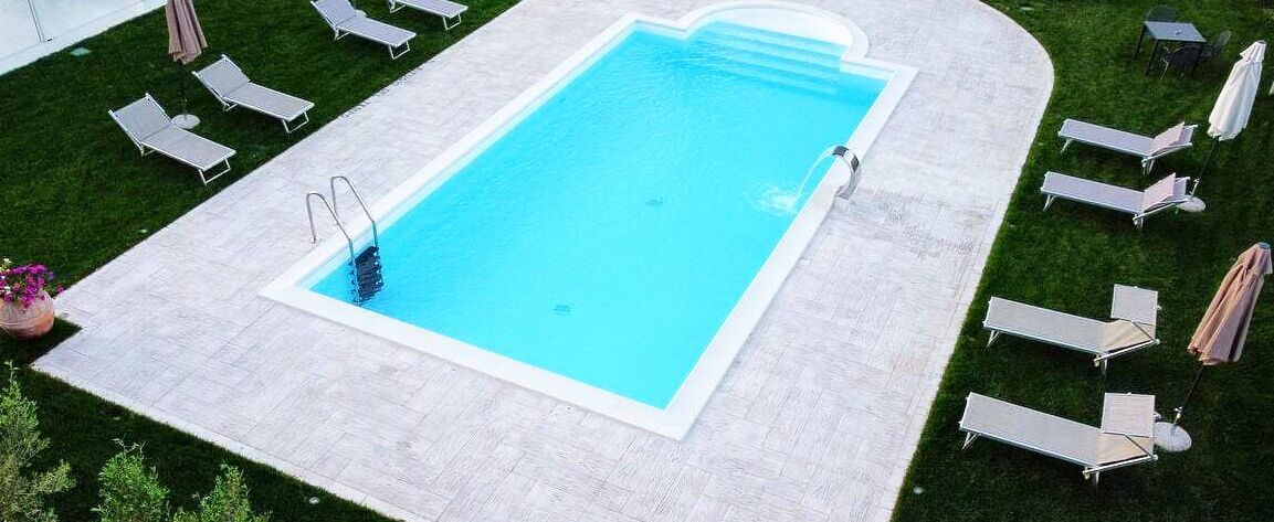 Une piscine rectangulaire bordée de blanc, entourée d’une terrasse dallée et d’une pelouse verdoyante.