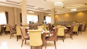 A restaurant with multiple dining tables and chairs, a bar area, and a kitchen in the background.