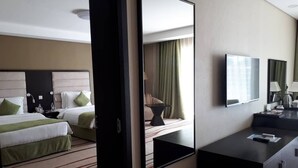 A hotel room with two beds, a large mirror, a flat-screen TV, and a desk with a lamp.