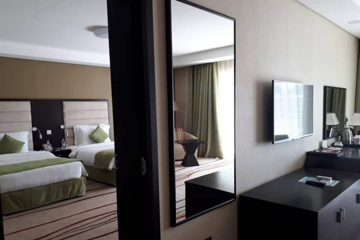 A hotel room with two beds, a large mirror, a flat-screen TV, and a desk with a lamp.
