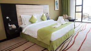 Habitación de hotel con una cama grande, teléfono junto a la cama, minibar y vista al exterior a través de un amplio ventanal.