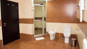 Un baño con una puerta negra, una ducha con puerta de vidrio, un bidé, un inodoro y un cubo de basura.
