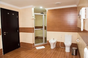 A bathroom with a black door, a shower with a glass door, a bidet, a toilet, and a trash bin. - Crossroads Hotel Blantyre (Blantyre)
