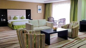 A hotel room with a bed, a sofa, two striped armchairs, a coffee table, and a small table with a lamp.