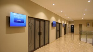 A hotel corridor with a digital display on the wall, glass railings, and a 'NO EXIT' sign.