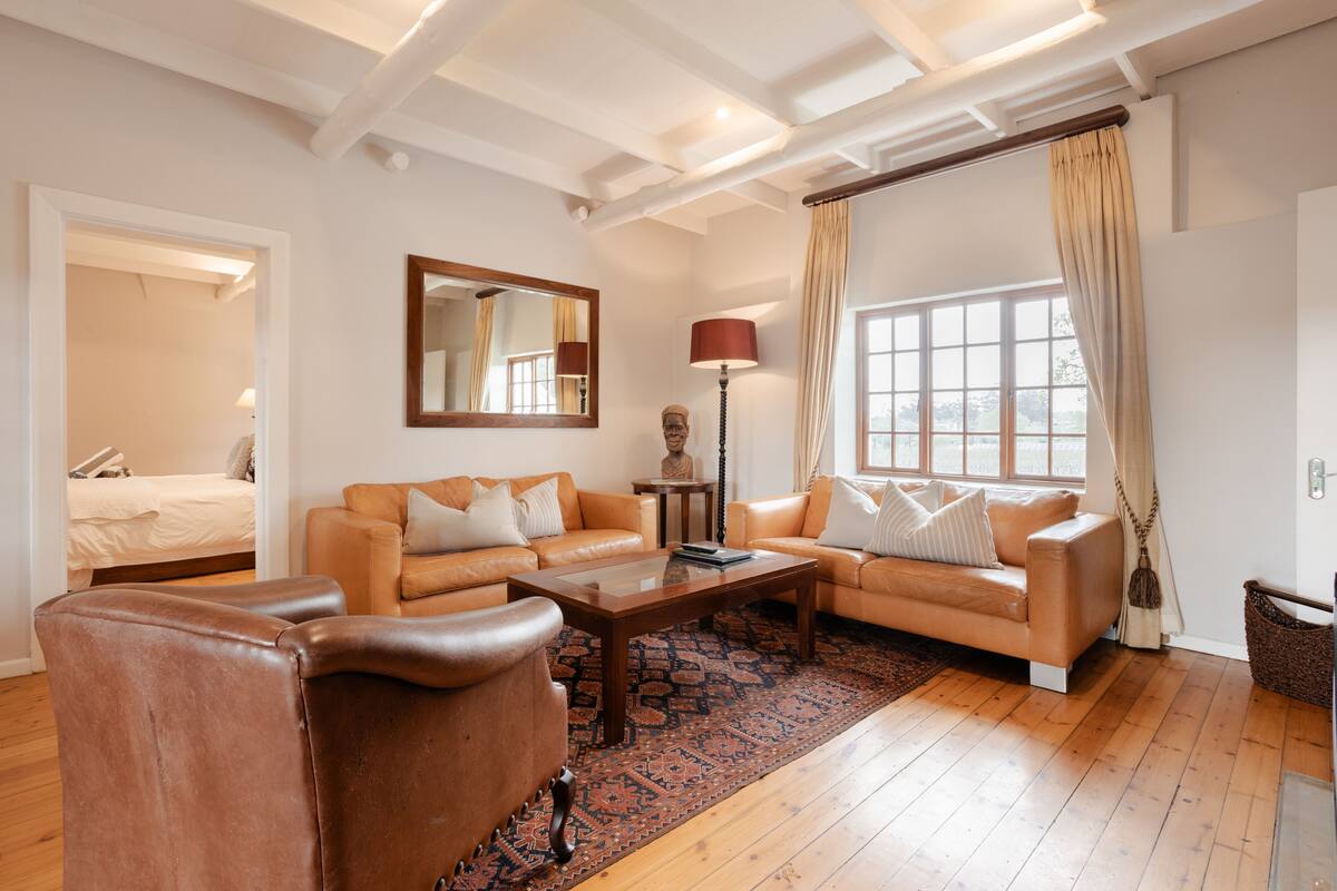A living room with a sofa set, a coffee table, a lamp, a mirror, and a window with curtains.