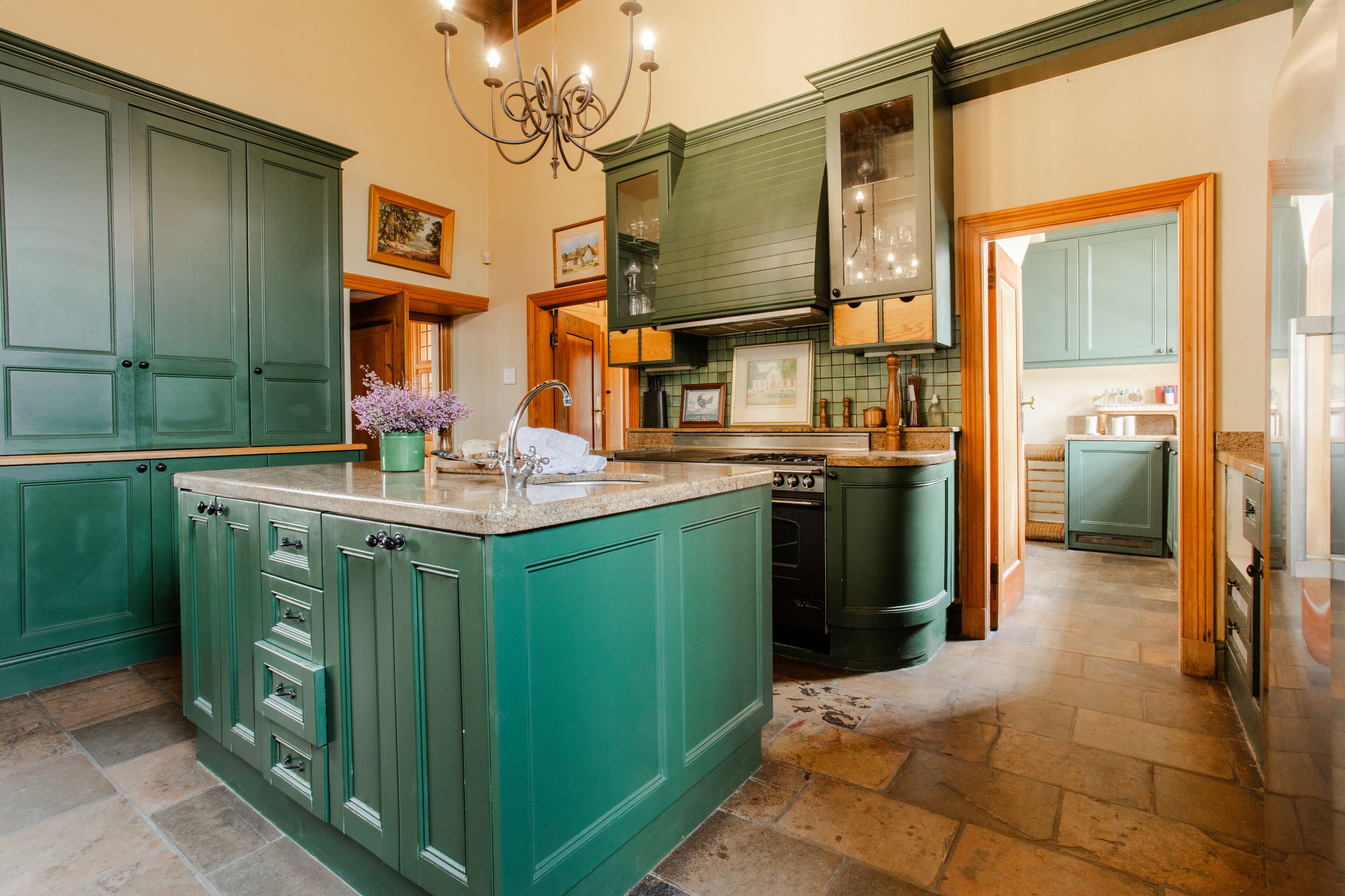 Une cuisine spacieuse avec des meubles de couleur verte, un grand îlot central et un évier intégré à l’îlot.