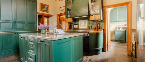 Une cuisine spacieuse avec des meubles de couleur verte, un grand îlot central et un évier intégré à l’îlot.
