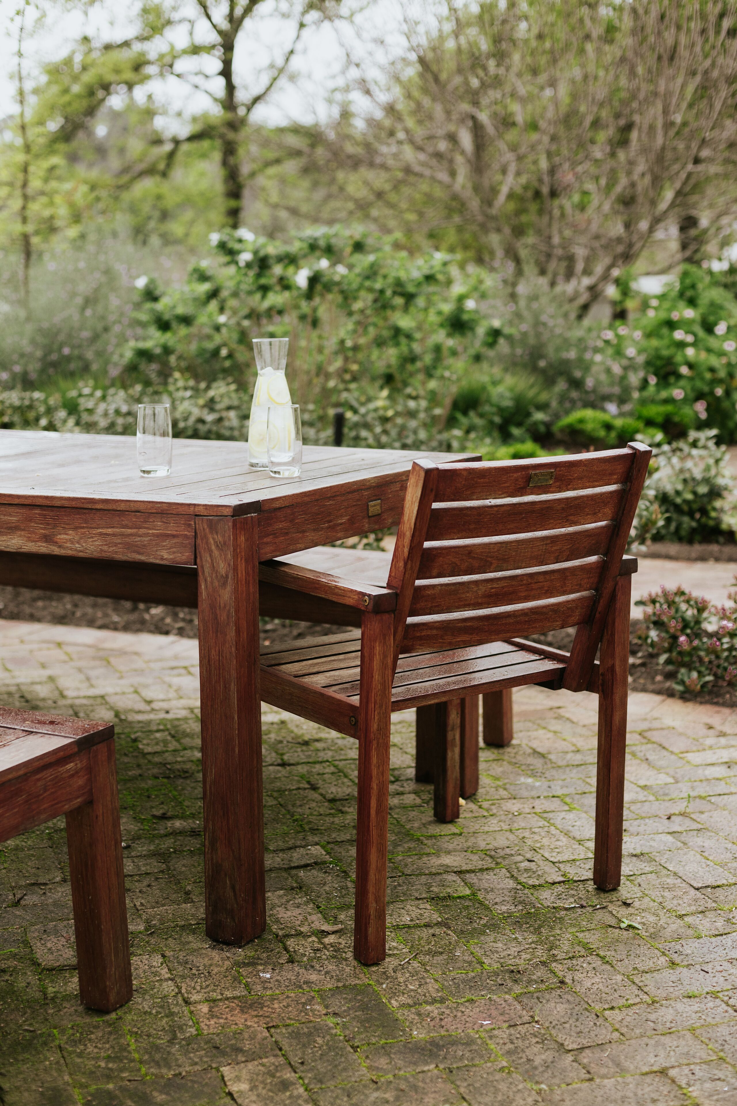 A wooden outdoor table with chairs, a glass, and a bottle.