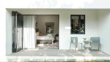 A modern bedroom with a bed, a window, and a small seating area with chairs and a table.