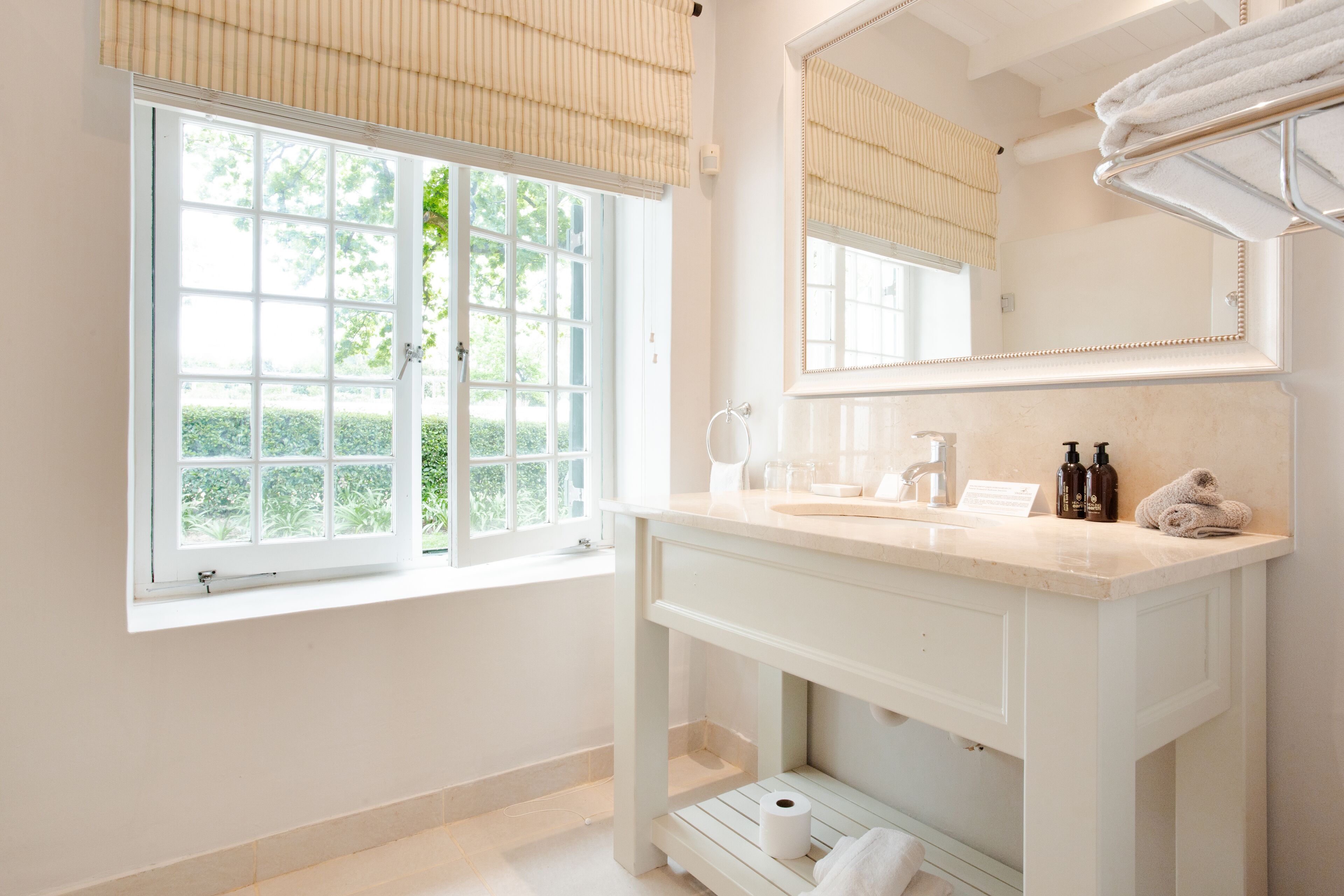 A bathroom with a large window, a vanity with a mirror, and a towel rack.
