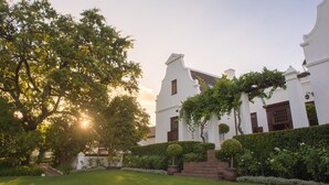 A white building with a garden and a large tree in front.