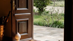 A wooden door with a brass handle, leading to a garden with a large tree and a view of a vineyard.