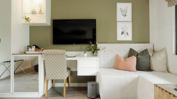 A modern living room with a white sofa, a desk with a computer, a TV, and framed botanical prints on the wall.