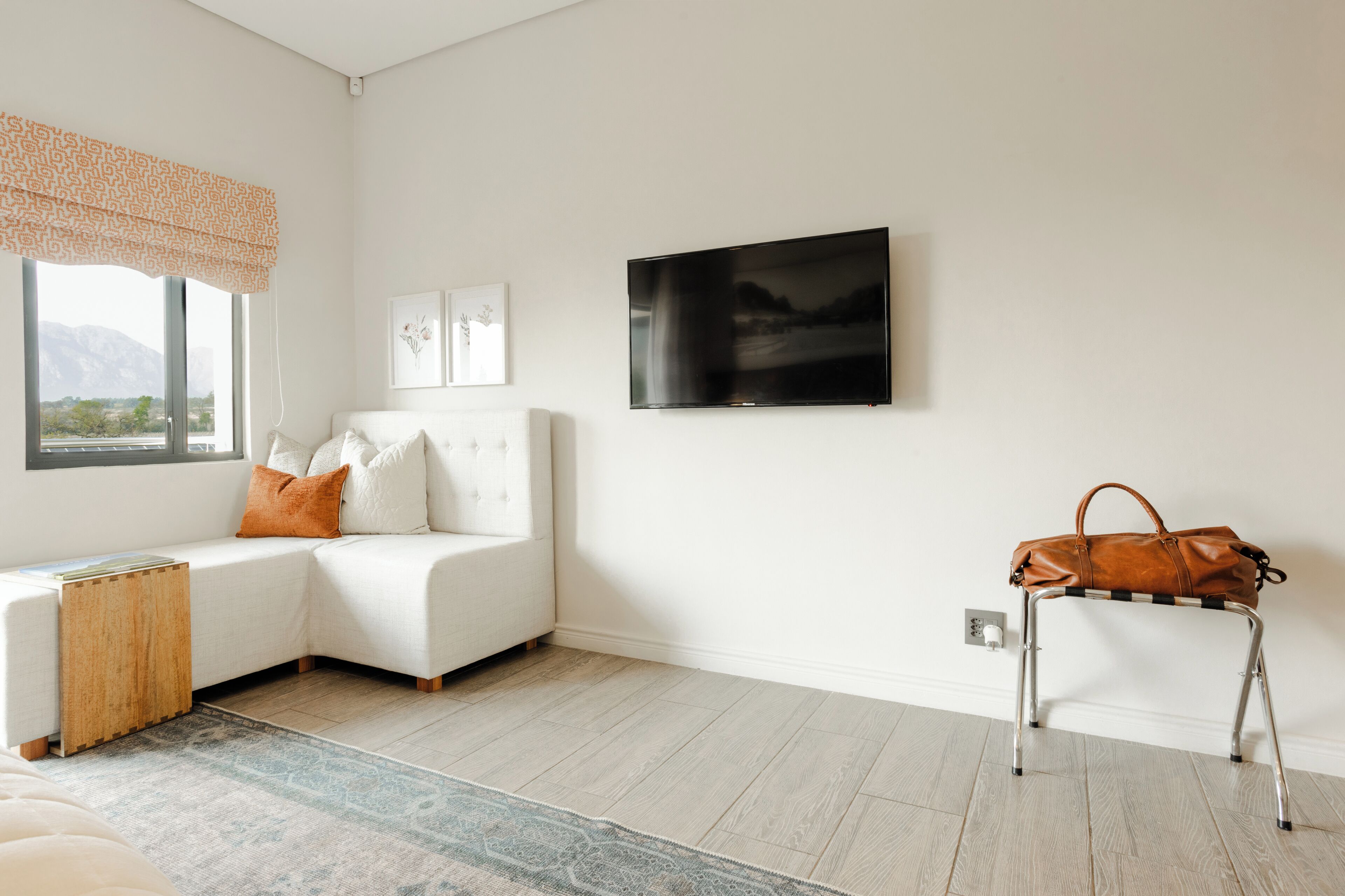 A modern living room with a white sofa, a mounted TV, and a leather bag on a metal stand.