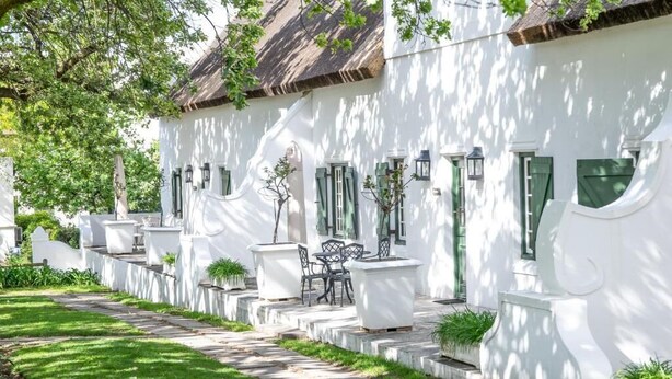 A white building with a thatched roof, outdoor seating, and a stone pathway.