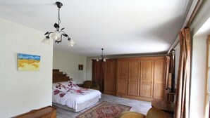 Um quarto com cama, guarda-roupa de madeira, cadeira, cômoda e lustre.