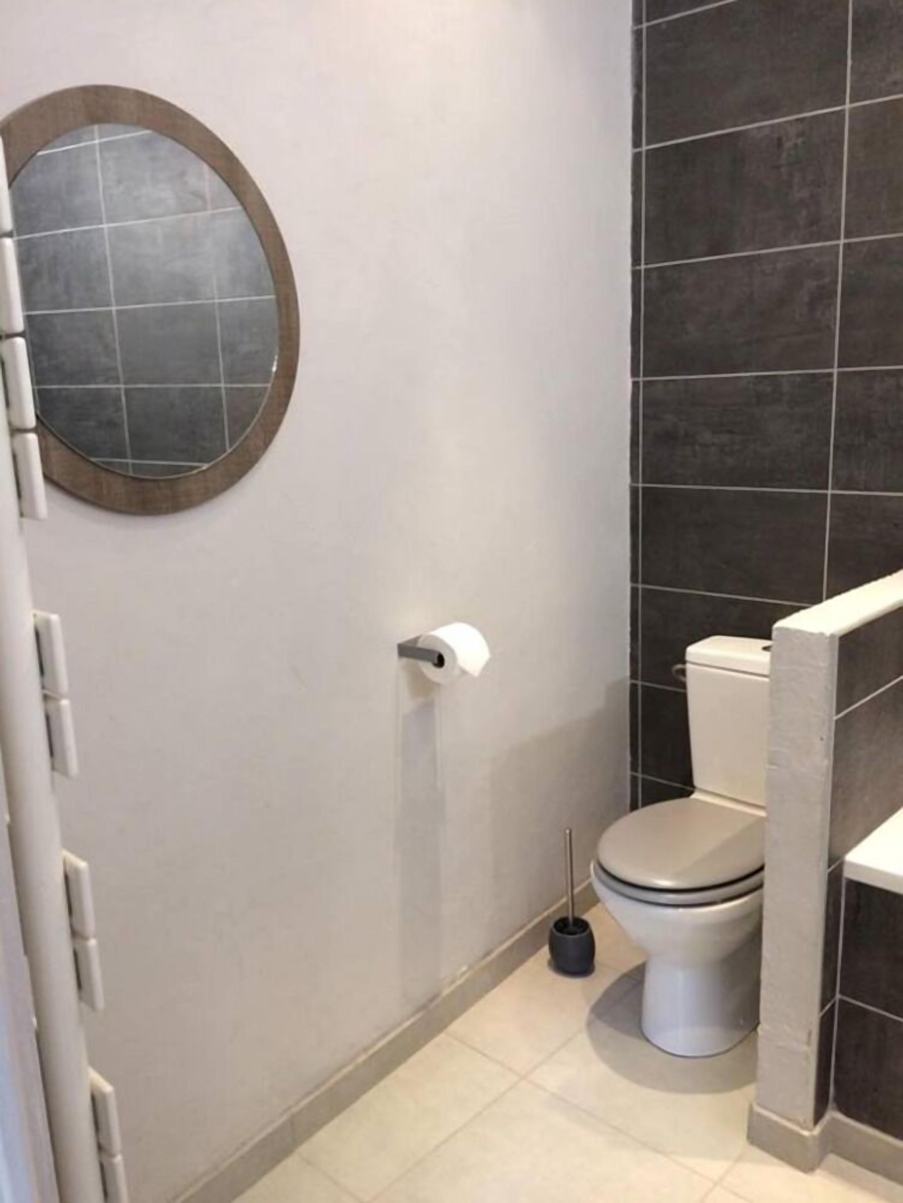 A bathroom with a toilet, a bidet, a toilet paper holder, and a round mirror on the wall.
